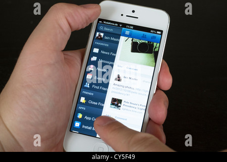 Close-up detail of man holding new iPhone 5 smart phone showing Facebook app and Timeline for user Stock Photo