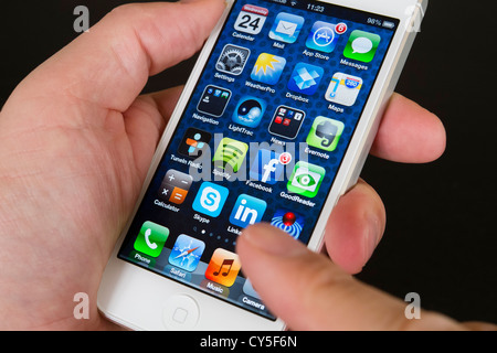 Close-up detail of man holding new iPhone 5 smart phone showing screen with many apps Stock Photo