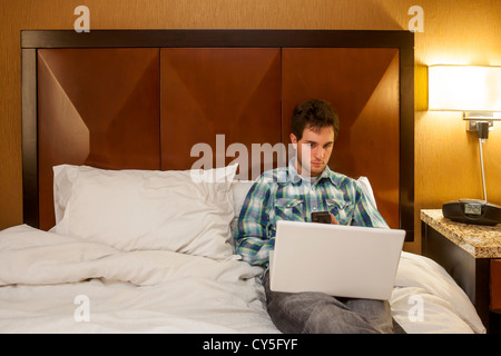 A young man relaxing on his bed and using his laptop computer. Stock Photo