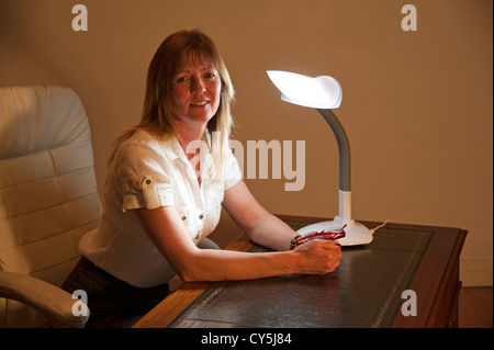 Woman and SAD table lamp. Seasonal Affective Disorder sufferer sitting at a desk Stock Photo