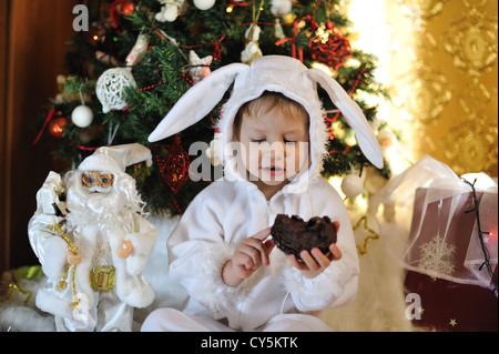 Node Christmas tree sits a boy dressed as a white rabbit Stock Photo