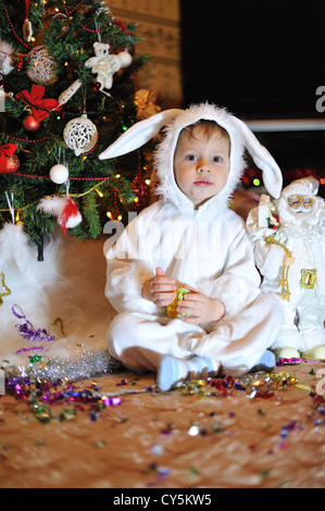 Node Christmas tree sits a boy dressed as a white rabbit Stock Photo