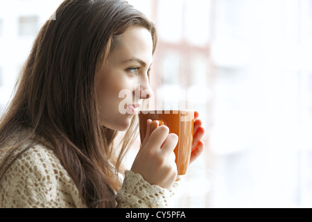 Beautiful young girl drinking hot tea while looking at the window Stock Photo