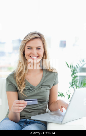 Woman using her credit card and laptop on the couch while smiling Stock Photo