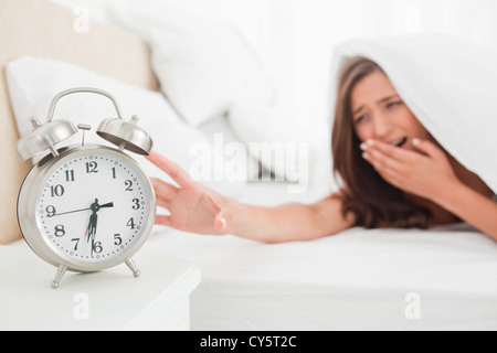 Woman yawning and reaching out for alarm clock from under her blanket Stock Photo