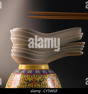 Pile of Chinese soup spoons on top of patterned bowl with wooden chopsticks Stock Photo