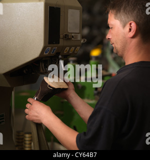 adult man working in a shoe factory, sewing the soles of the shoes, at a machine Stock Photo