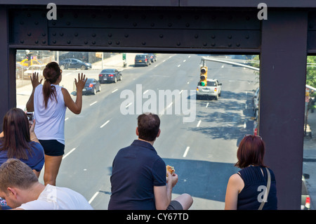 Tourists enjoy the viewing window on the High Line city park, looking north up 10th Avenue, Manhattan, New York. Stock Photo