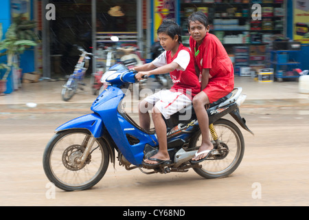 Two boys brave the elements on a motorbike in Sisophon, Cambodia Stock Photo