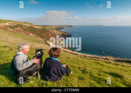 A couple and their dog enjoying the view on the South Devon coastal path east of Plymouth on a late sunny summer evening. UK Stock Photo