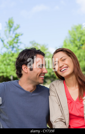 Man looking his friend as she is laughing joyfully while sitting in a park Stock Photo