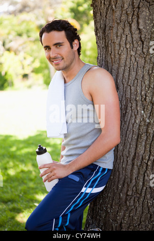 Smiling man looking to the side while holding a sports bottle and resting Stock Photo