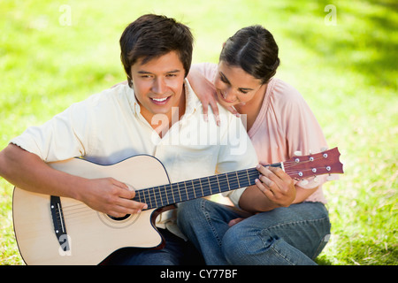 Woman leaning while leaning on her friends shoulder as he plays the guitar Stock Photo