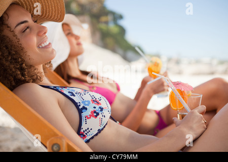 Smiling young woman sitting in a deck chair while holding her cocktail Stock Photo