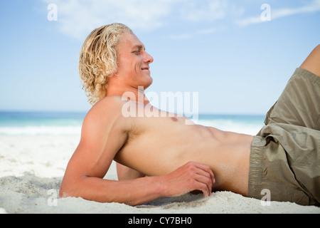 Side view of a blonde man lying on the beach Stock Photo