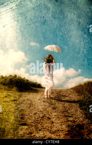 a girl in a white dress is walking in the dunes with a parasol Stock Photo