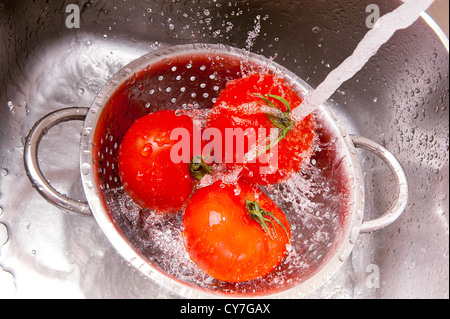 Fresh vegetables under water stream in colander Stock Photo