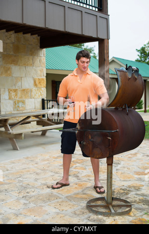 Young man is about to barbecue while enjoying a glass of red wine Stock Photo