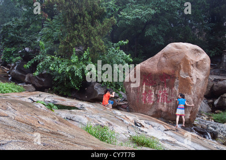 Two girls pose next to a huge boulder and its inscription on Mount Tai in Shandong Province, China Stock Photo