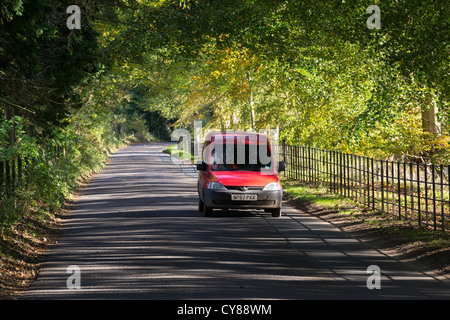 Sunlight shining through trees onto a road giving dappled and striped shadows, and a red post van Stock Photo