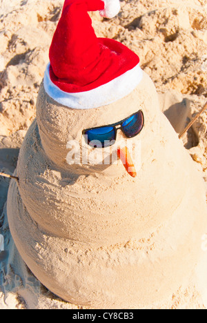 Perfect Sandman With Carrot Nose And Sunnies, perfectly shaped Snowman made from sand with Santa hat. Stock Photo