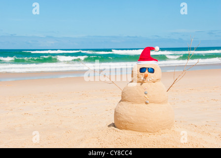 Perfect Sandman With Carrot Nose And Sunnies, perfectly shaped Snowman made from sand with Santa hat. Stock Photo