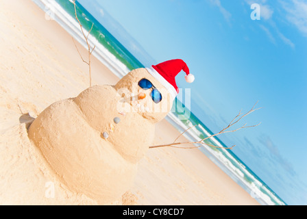 Perfect Sandman With Carrot Nose And Sunnies, perfectly shaped Snowman made from sand with Santa hat. Stock Photo