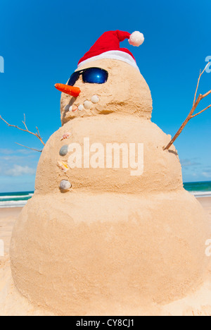 Perfect Sandman With Carrot Nose And Sunnies, perfectly shaped Snowman made from sand with Santa hat. Stock Photo