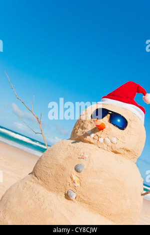 Perfect Sandman With Carrot Nose And Sunnies, perfectly shaped Snowman made from sand with Santa hat. Stock Photo