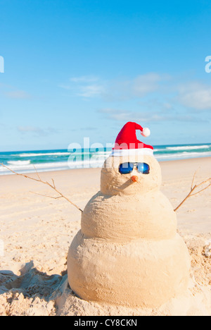 Perfect Sandman With Carrot Nose And Sunnies, perfectly shaped Snowman made from sand with Santa hat. Stock Photo