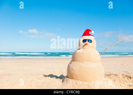 Perfect Sandman With Carrot Nose And Sunnies, perfectly shaped Snowman made from sand with Santa hat. Stock Photo