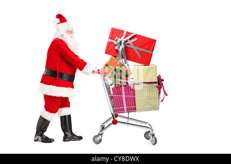 Santa Claus standing next to a shopping cart full of gifts isolated on white background Stock Photo