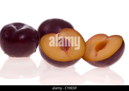Plum cut in two haves photographed on a white background. Two whole plums in the background. Stock Photo