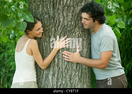 Young couple leaning against tree trunk, smiling at each other Stock Photo
