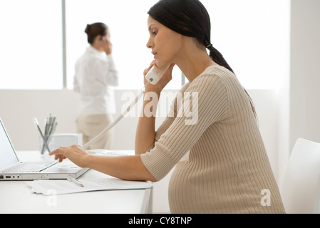 Young pregnant woman talking on landline phone in office, backlit Stock Photo