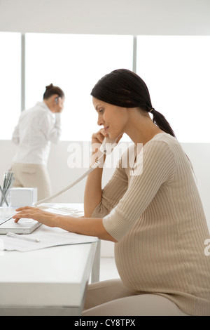 Young pregnant woman talking on landline phone in office, backlit Stock Photo