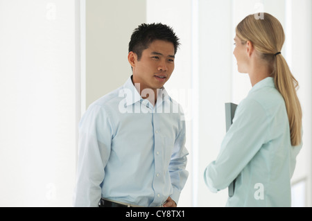 Mid-adult man talking to female colleague in office corridor Stock Photo