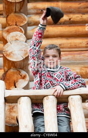 Boy standing on deck of log cabin, waving hat at camera, portrait Stock Photo