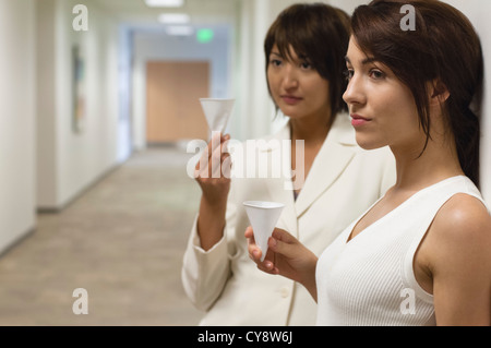 Businesswomen taking break and drink from disposable cups in hallway Stock Photo