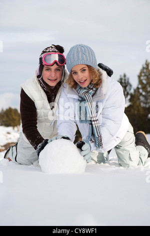 Teenage girls rolling snowball together, portrait Stock Photo