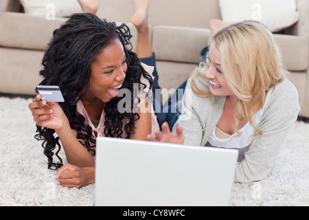 A woman holding a bank card is lying on the ground next to her smiling friend Stock Photo
