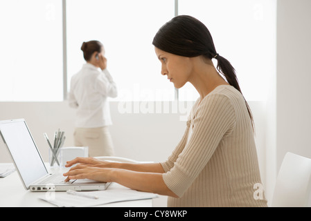 Young pregnant woman typing on laptop computer in office, backlit Stock Photo