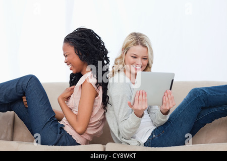 Two laughing women sitting back to back have a tablet computer Stock Photo
