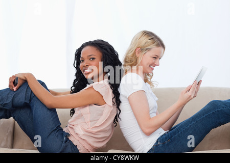 Two happy women are sitting on a couch back to back Stock Photo