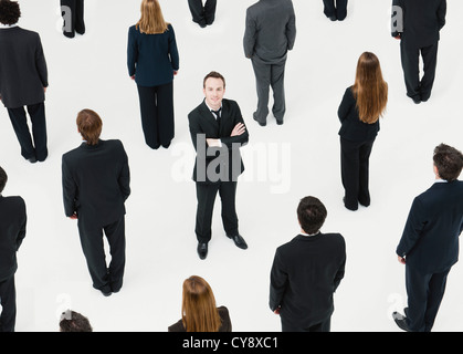 Businessman with arms crossed standing in midst of anonymously dressed business professionals Stock Photo