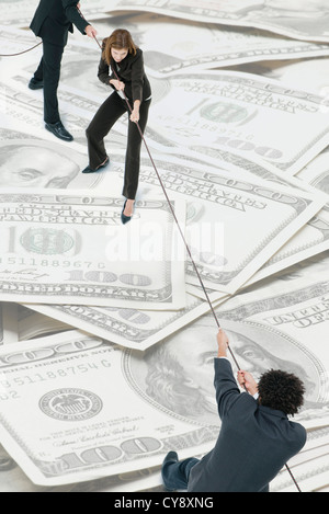 Executives playing tug-of-war on top of pile of one-hundred dollar bills Stock Photo