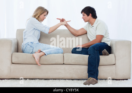 A couple sitting on a couch are pointing at each other Stock Photo