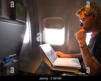 Mature Man Works on Laptop Computer Aboard Airplane Inflight Stock Photo