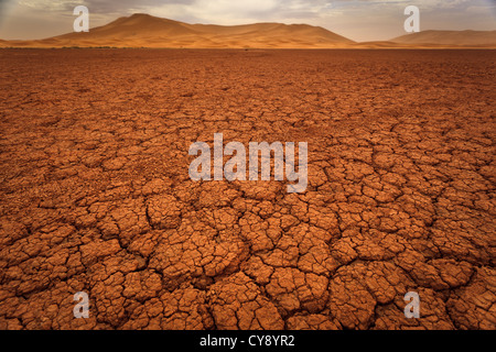 Cracked pattern of dry lake bed red mud and sand dunes in Sahara Desert Morocco Stock Photo