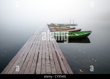 Autumn. Small pier with boats on lake in cold still foggy morning Stock Photo